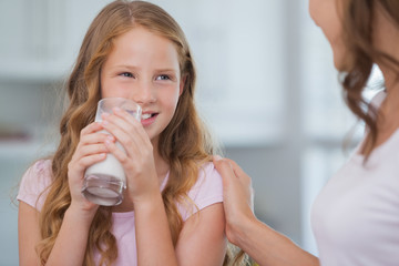 Wall Mural - Cute girl drinking milk as she looks to her mother