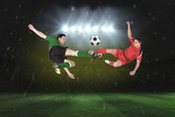 Fototapeta Sport - Football players tackling for the ball against football pitch under spotlights