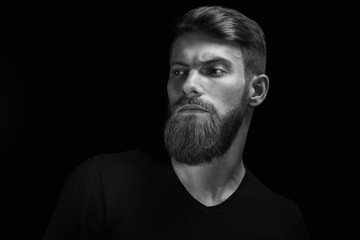 Wall Mural - Portrait of handsome single bearded young man with serious expression looking over black background with copy space