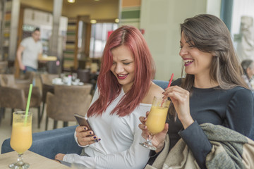 Portrait of two young beautiful women using mobile phone at coffee shop.