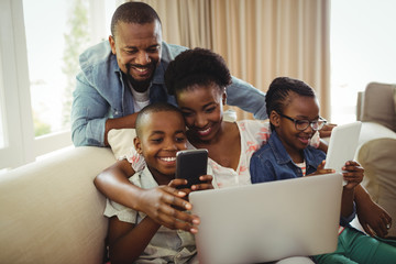 Wall Mural - Parents and kids using laptop, smartphone and digital tablet on sofa