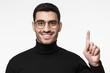 © Damir Khabirov - Indoor photo of young European man in total black isolated on white background looking through eyeglasses, pointing upwards with finger as if having found interesting idea or creative solution