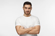 © Damir Khabirov - Closeup photo of young strong European Caucasian man pictured isolated on grey background dressed casually, standing with arms crossed and serious concentrated face at camera, looking aggressive