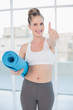 © WavebreakmediaMicro - Sporty blonde holding balled up exercise mat giving thumb up