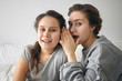 © Anatoliy Karlyuk - Indoor shot of attractive young Caucasian woman in gray casual sweatshirt telling secret to her teenage sister, whispering into her ear and looking at camera, having mysterious suspicious expression