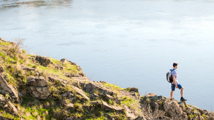 Wall Mural - young man traveler with backpack enjoing landscape on beautiful rock at sunny evening. travel and ad