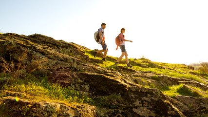 Young Happy Couple Hiking with Backpacks on the Beautiful Rocky Trail at Sunny Evening. Family Travel and Adventure.