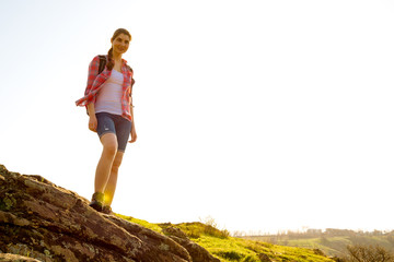 Wall Mural - Portrait of Happy Woman Traveler with Backpack Standing on the Rock at Sunny Evening. Travel and Adventure Concept.