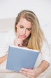 © WavebreakmediaMicro - Concentrated model using her tablet lying on cosy bed