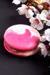 © alexmishchenko - A beautiful, fashionable, unusual, magical macaron \ macaroon with a delicate cream filling. Expensive French dessert made from almond flour on a black background. Sakura branch for decoration.