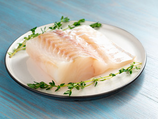 piece of raw cod fish fillet on plate on blue wooden table, side view