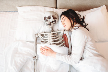 Woman sleeping in bad with funny human skeleton