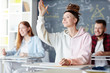 Clever teenage student in hoodie raising her hand at lesson to answer question of teacher