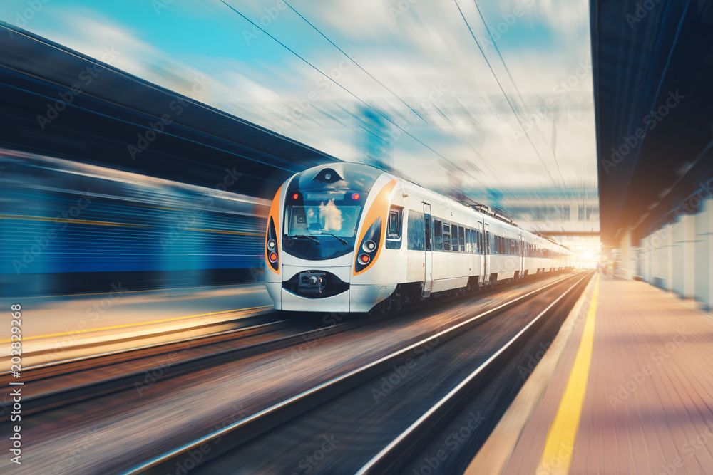 High speed passenger train in motion on the railway station at sunset in Europe. Modern intercity train on railway platform with motion blur effect. Urban scene with railroad. Railway transportation - obrazy, fototapety, plakaty 