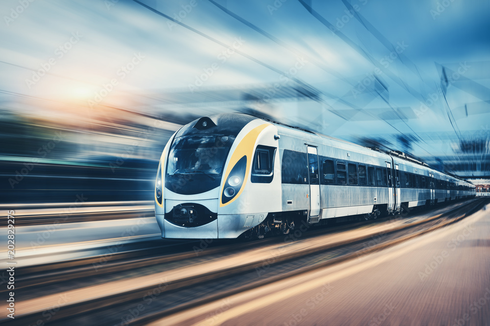 High speed passenger train in motion on the railway station at sunset in Europe. Modern intercity train on railway platform with motion blur effect. Urban scene with railroad. Railway transportation - obrazy, fototapety, plakaty 