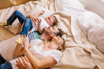 Young couple with their daughter are laughing while they lying on bed in bedroom