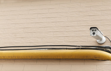 Outdoor surveillance camera on a brick pale pink wall.