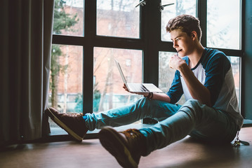 Student sits on the floor with laptop and reads something