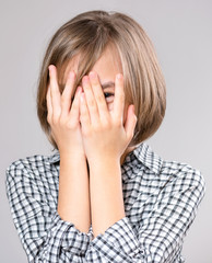 Close-up emotional portrait of caucasian charming girl smiling to you shyly, covered her face on gray background.