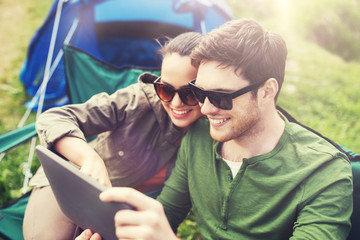 Canvas Print - travel, hiking, technology, tourism and people concept - smiling couple with tablet pc computer sitting on chairs at camping tent