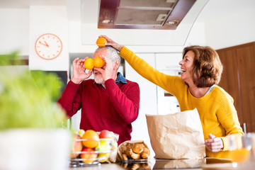 Wall Mural - Senior couple unpacking food in the kitchen, having fun.