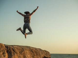 jumping WOMAN celebrates her triumph WITH arms up on top of a rock at the beach