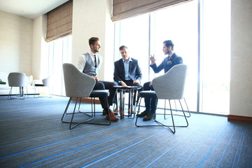 Mature businessman using a digital tablet to discuss information with a younger colleague in a modern business lounge.