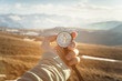 a man's hand holds a hand-held compass against the backdrop of mountains and hills at sunset. The concept of travel and navigation in open areas