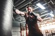 Bearded Male boxer training with punching bag in dark sports hall. Young tattoed boxer training on punching bag. Male boxer as exercise for the big fight. Boxer hits punching bag.