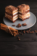 Wall Mural - Sweet dessert tiramisu in a cut on a gray plate on a black wooden background with spices: cinnamon sticks and badan, coffee beans