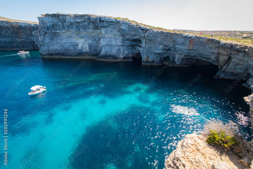 Exploring the dramatic huge cliffs and sea caves of east coast of Comino, over looking the deep azure crystal clear waters of the Mediterranean, Comino, Malta, June 2017 - obrazy, fototapety, plakaty 