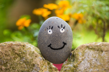 Rounded stone pebble, with smiley face painted on it, over rocks in garden