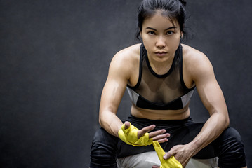 Asian female boxer wearing yellow strap on wrist. Beautiful young woman with muscular body preparing for boxing