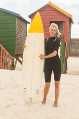 Wall Mural - Portrait of happy woman standing with surfboard while standing against huts