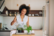 © chika_milan - Beautiful mixed race woman gardening fresh herbs at her kitchen.