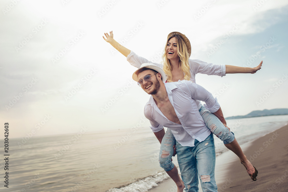 Happy couple in love on beach summer vacations. Joyful girl piggybacking on young boyfriend having fun. - obrazy, fototapety, plakaty 