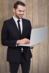 Wall Mural - Smiling businessman standing and using laptop against wooden surface with planks