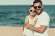 © VadimGuzhva - Young father in sunglasses hugs daughter on beach near sea.