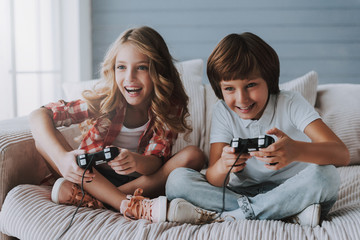 Joyful children with game controllers play video games at home.