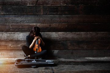 The lady is sitting on grunge surface cement floor,hold violin and bow in her arms,turn face down to volin,vintage and art style,blurry light around.