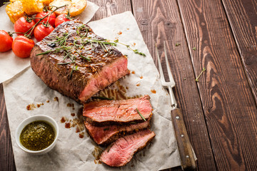 Wall Mural - Sliced Roast beef on white paper on wooden table with grilled vegetables. Copyspace