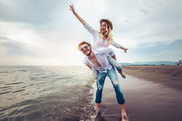 Happy couple in love on beach summer vacations. Joyful girl piggybacking on young boyfriend having fun.