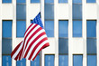 An American flag is waving on a blurred blue building full of windows in Manhattan, New York, United States.