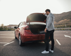 Man traveler putting suitcase in car trunk