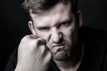 Portrait Of An Angry Man Clenching His Fist On A Black Background. Family Conflicts And Violence. The Concept Of Aggression