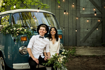 Cheerful happy young couple sit on the bumper retro-minibus.