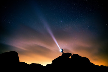 man posing with flashlight on hill top in early morning in front of stars and milky way