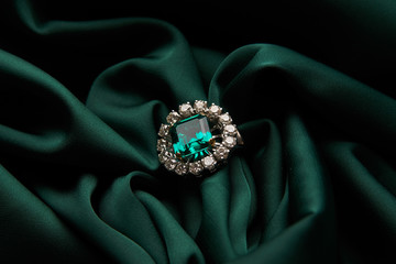 Wall Mural - Green emerald fashion engagement diamond ring on green satin background. Luxury female jewellery, close-up. Selective focus