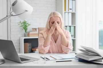 Canvas Print - Mature woman suffering from headache while sitting at table in office