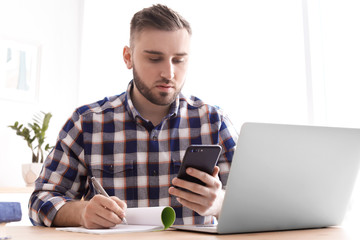 Wall Mural - Young man working with mobile phone and laptop at desk. Home office